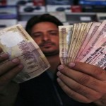 A shopkeeper poses for a picture as he counts Indian currency notes at his shop in Jammu